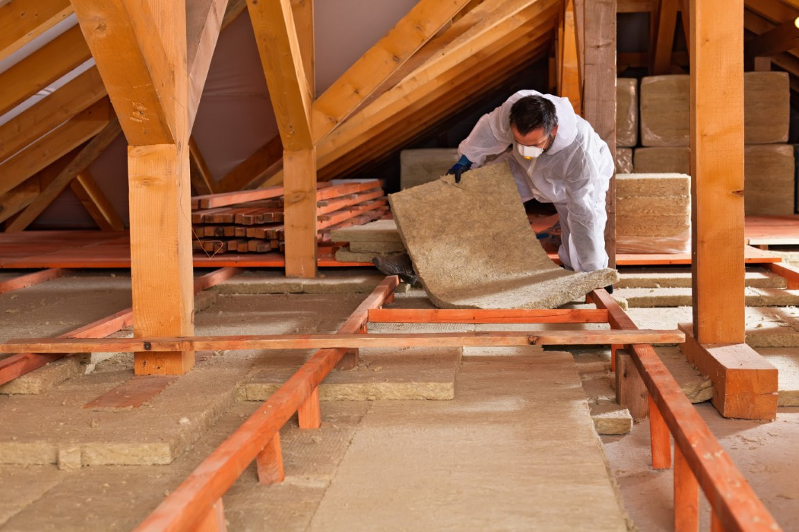 A picture of a man placing insulation materials at the attic